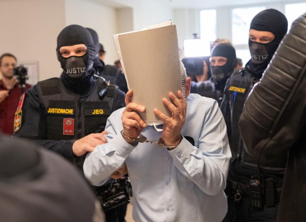 Former Syrian general defendant Khaled Al-Halabi covers his face as he is escorted in handcuffs to the courtroom by justice officers for the trial at the Regional Vienna’s Court of Austria in Vienna, Austria, on June 1, 2026. (AFP)