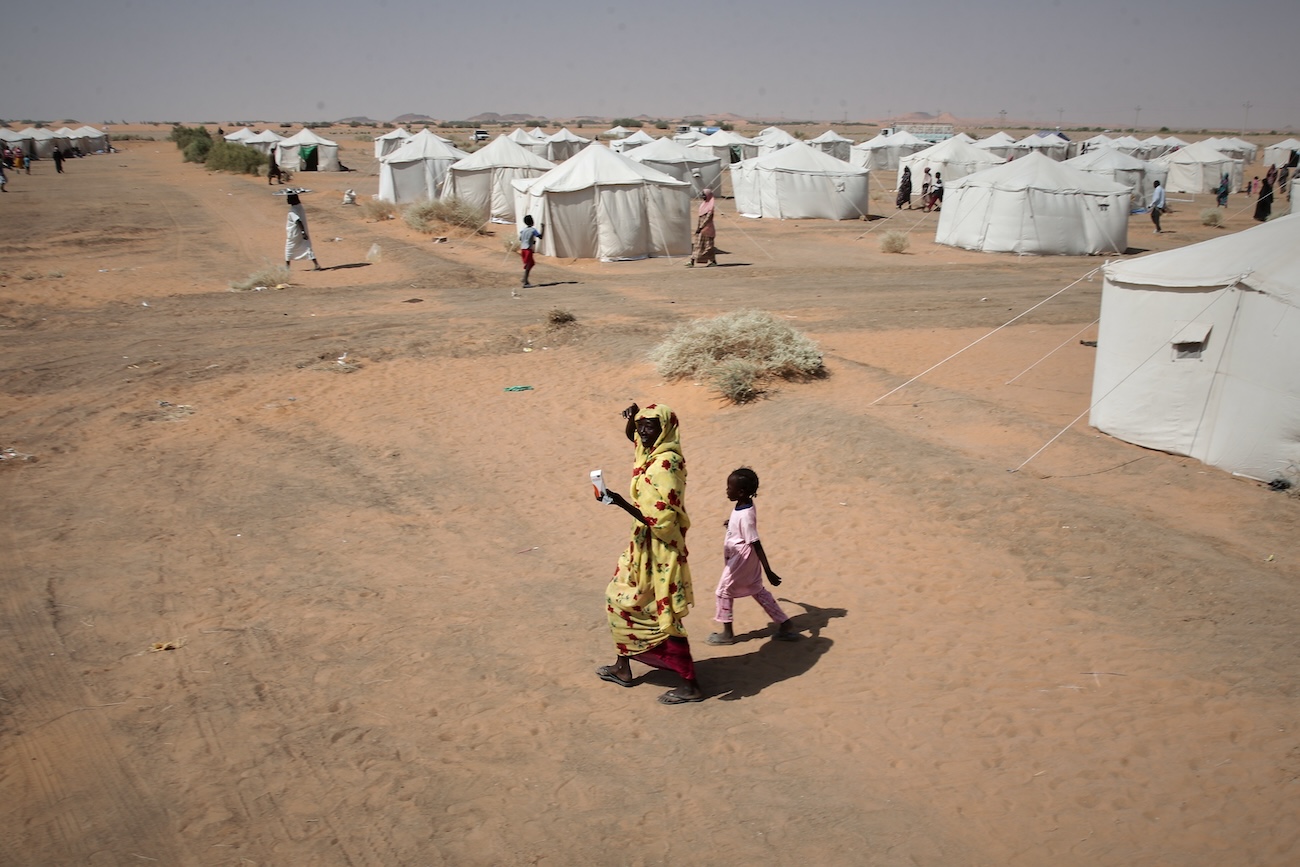 A woman and child, displaced from North Darfur’s capital, El-Fasher or other conflict-affected areas walk in the newly established El-Afadh camp in Al Dabbah, in Sudan’s Northern State. (File/AP)