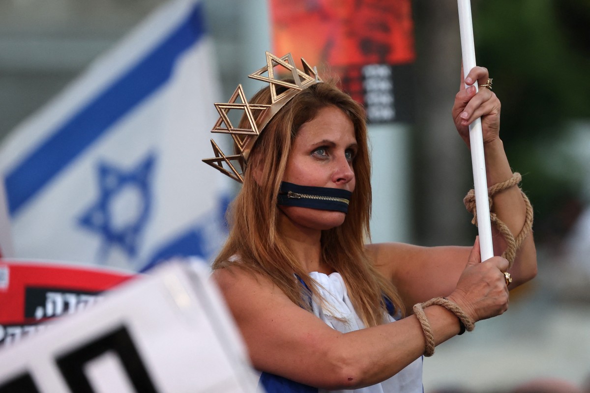 A woman stands with a symbolic zipper covering her mouth and ropes around her hands as Israeli protesters rally against the government and the war in Gaza at Hostage Square in Tel Aviv, July 2, 2026. (AFP)