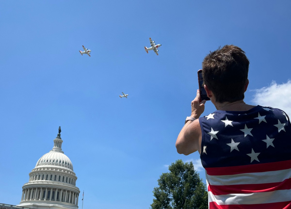 A woman films US Coast Guard fixed-wing turboprop planes flying over the US Capitol as part of the ‘Salute to America’ Independence Day celebration on the National Mall in Washington, DC, Jul. 4, 2026. (AFP)