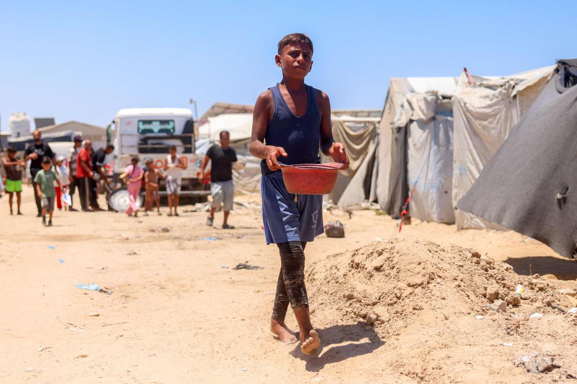 A boy walks with a pot past tents for people displaced by war in Khan Yunis in the southern Gaza Strip on July 11, 2026. In spite of the ongoing risk of renewed fighting in Gaza, stakeholders have spent months preparing for the post-war phase. (AFP)