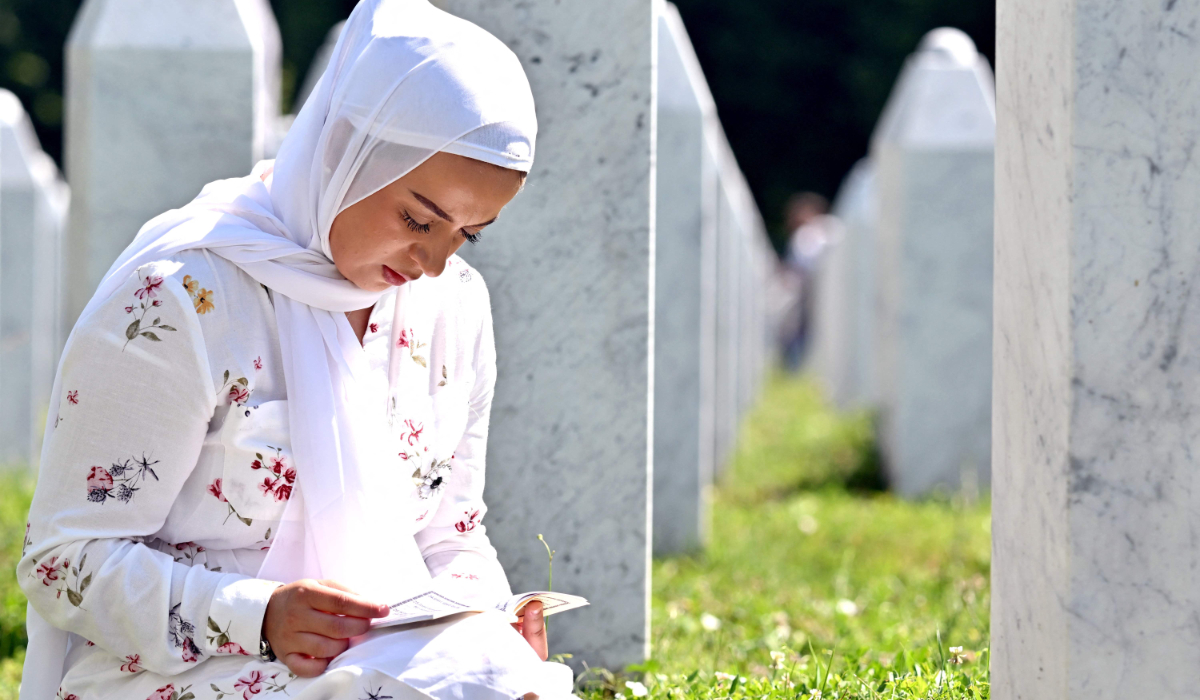 A Bosnian Muslim woman reads from a book of prayers beside the gravestones of her relatives, at the memorial cemetery in village of Potocari, near Eastern-Bosnian town of Srebrenica, on July 11, 2026, marking the 31st anniversary of Srebrenica genocide. (AFP)