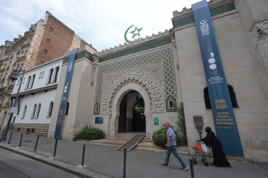 People walk past the Grand Mosque of Paris, where a banner reads, "100 years of light, a century of history, spirituality and dialogue" marking its 100th anniversary in France. (AP)