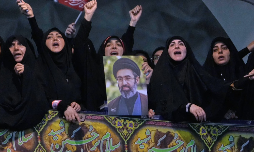 Mourners chant slogans as one of them holds a poster of the Supreme Leader, Mojtaba Khamenei, in a ceremony commemorating the late Supreme Leader, Ali Khamenei, in Tehran, Tuesday, July 14, 2026. (AP)