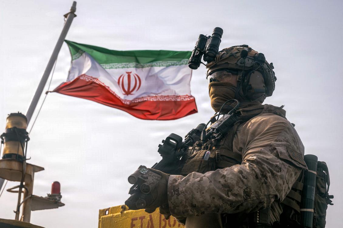 This US Marine Corps handout photograph taken on July 16, 2026, by US Central Command Public Affairs reportedly shows an Iranian flag flying behind a US Marine from the 11th Marine Expeditionary Unit during a verification boarding aboard M/T Wen Yao in the Gulf of Oman. (Photo by Sgt. Joseph Helms / US MARINE CORPS / AFP)