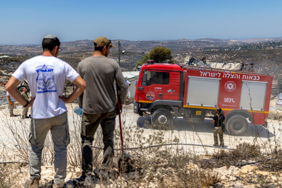 Israeli settlers stand near a firetruck as they inspect the aftermath of a fire that broke out the previous day in the Israeli settlement of Havat Gilad, adjacent to the Palestinian village of Tell in the occupied West Bank, July 19, 2026. (AFP)
