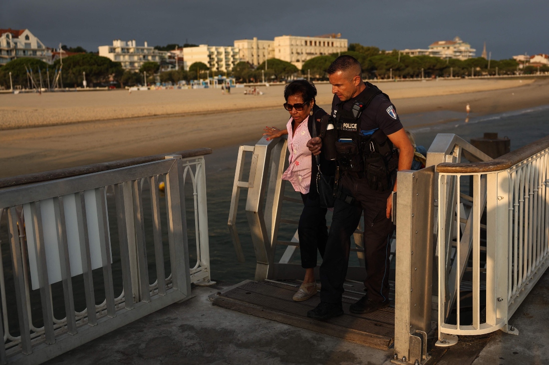 A police officer helps a holidaymaker from Lege-Cap-Ferret upon her arrival in Arcachon by boat during an evacuation operation of the entire Cap-Ferret peninsula, in southwestern France. (AFP)