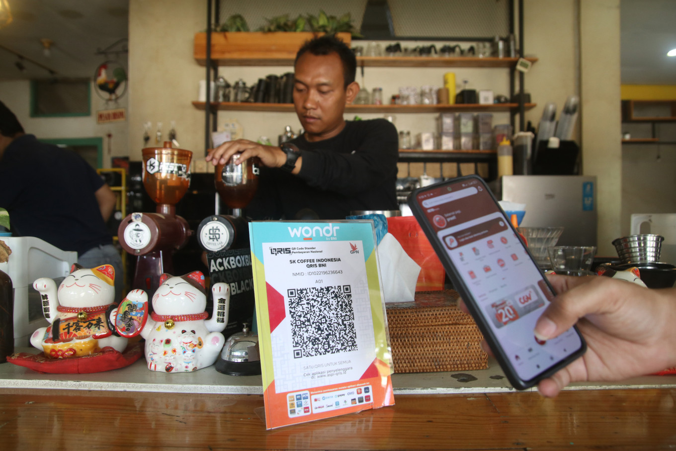 A barista prepares a beverage as a customer uses a smartphone to scan a Quick Response Indonesia Standard (QRIS) code to make a digital payment in Kediri, East Java on Sept. 19, 2024. (Antara)