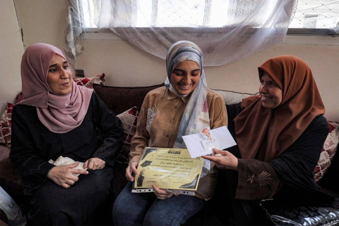 Palestinian high school student Saba Rabah (C), the top-ranked student in the science stream of the Palestinian national high school exams, celebrates with family at the Maghazi camp for Palestinian refugees in the central Gaza Strip on July 26, 2026. Just days before her final secondary school examinations, the house opposite Rabah's temporary home was bombed, prompting her and her family to flee leaving behind everything they had. (Photo by Eyad Baba / AFP)