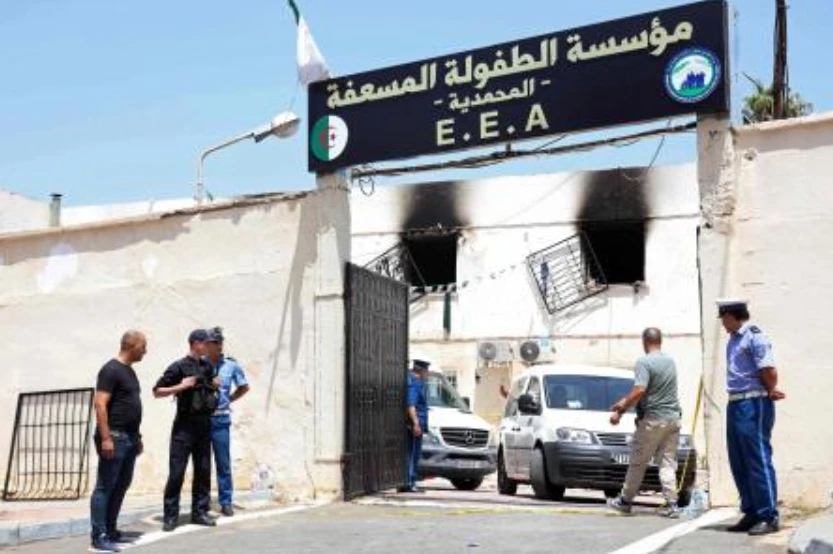 Police officers stand guard as vehicles leave through the entrance of an orphanage following a fire in the Mohammadia suburb of Algiers on July 16, 2026. (AFP)