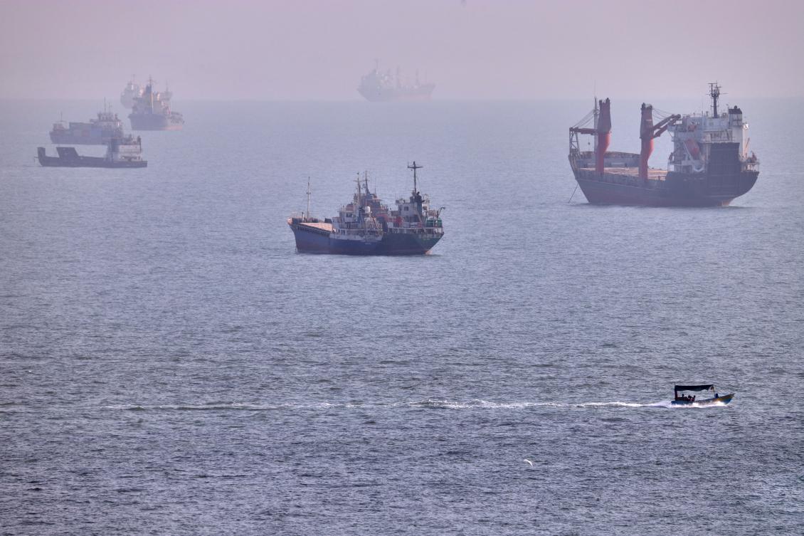 A small boat sails past cargo ships and other commercial vessels anchored in the Strait of Hormuz off Bandar Abbas, Iran. (File/AP)