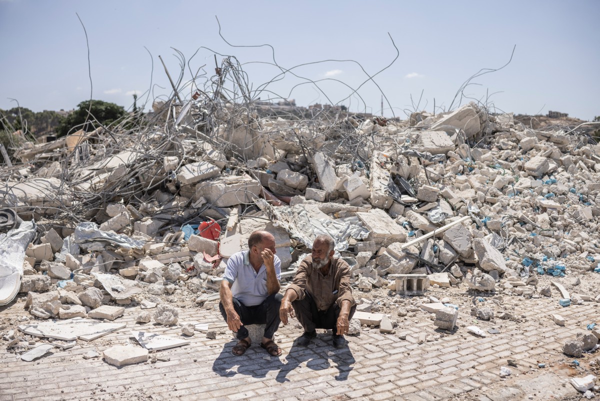 Two Palestinian men crouch amid the rubble of shops and apartments demolished by Israeli forces in Arraba, near Jenin, on July 27, 2026. (AFP)