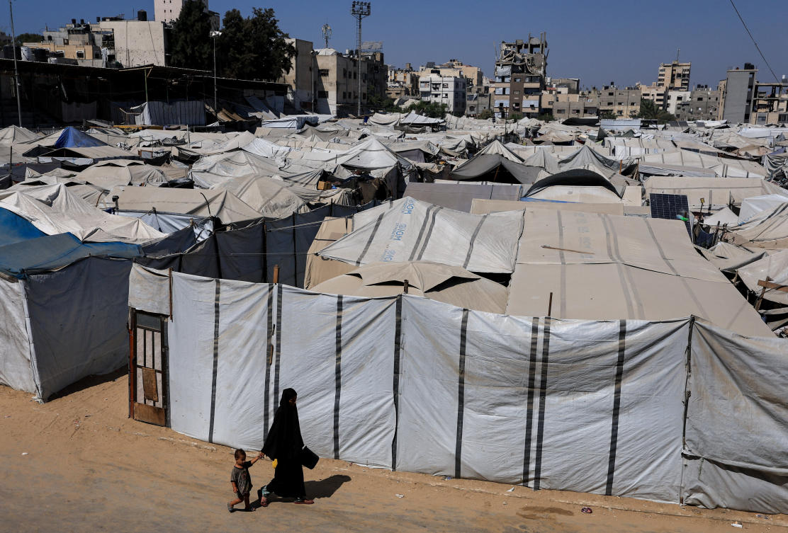 A Palestinian woman and a child walk next to a tent camp sheltering displaced Palestinians in Gaza City, August 9, 2026. (Reuters)