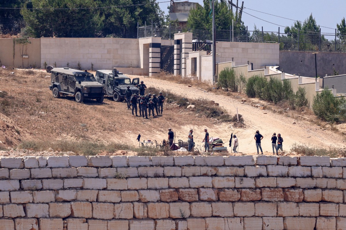 Israeli soldiers (top) stand guard next to settlers in front of the Palestinian houses in the village of Qusra, south of Nablus, on August 12, 2026. (AFP)