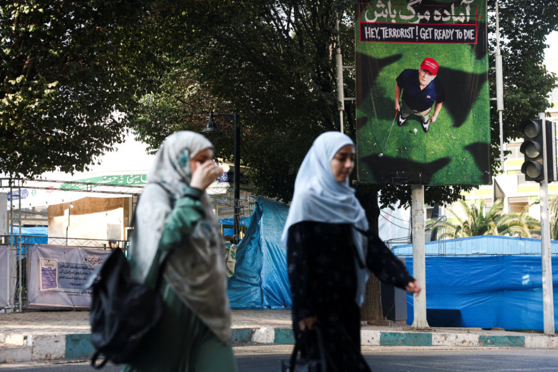 People walk near a banner depicting US President Donald Trump playing golf, on a street in Tehran, Iran, on August 13, 2026. (Majid Asgaripour/WANA via Reuters)