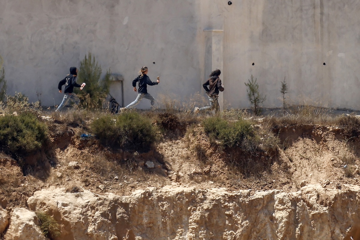 Israeli settlers run as being chased by an Israeli military vehicle around Palestinian houses in the village of Qusra, south of Nablus, in the occupied West Bank, on August 13, 2026. (FILE/AFP)