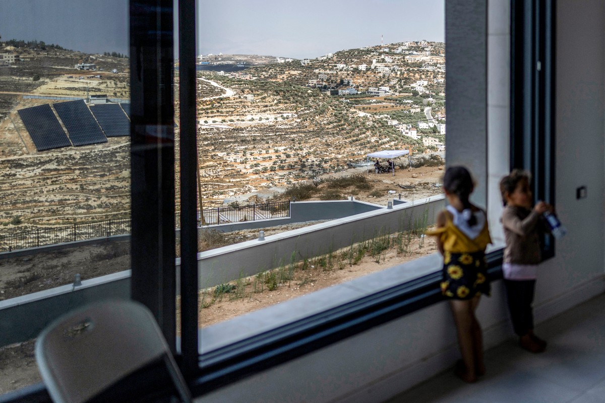 Palestinian children stand by an open window in one of the Palestinian homes besieged by Israeli settlers in the occupied West Bank village of Qusra. (File/AFP)
