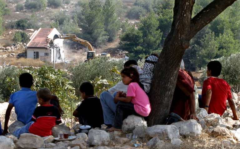 A Palestinian family watches an Israeli bulldozer demolishing houses in the northern West Bank settlement of Kadim, which was one of the four settlements evacuated in the West Bank as part of Israeli Prime Minister Ariel Sharon's disengagement plan. (File/AFP)