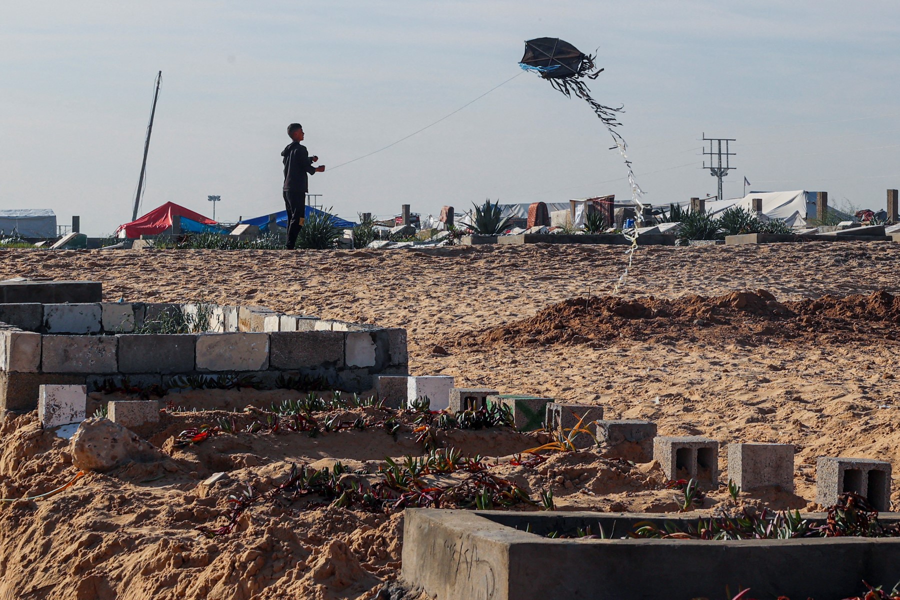 A youth flies a kite near graves prepared for Palestinians killed during overnight Israeli strikes at a cemetery in Rafah, in the southern Gaza Strip, Feb. 21, 2024. (AFP/File)