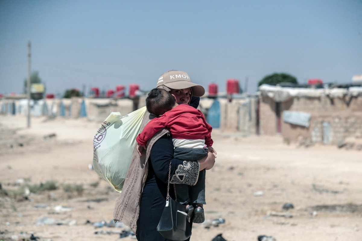 A displaced Syrian Kurdish woman carries a child at Al-Talaeh camp in Hasakeh, northeastern Syria, July 23, 2026. (AFP)