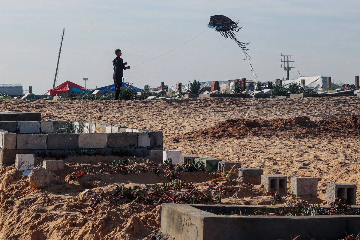 A youth flies a kite near graves prepared for Palestinians killed during overnight Israeli strikes at a cemetery in Rafah, in the southern Gaza Strip, Feb. 21, 2024. (AFP/File)
