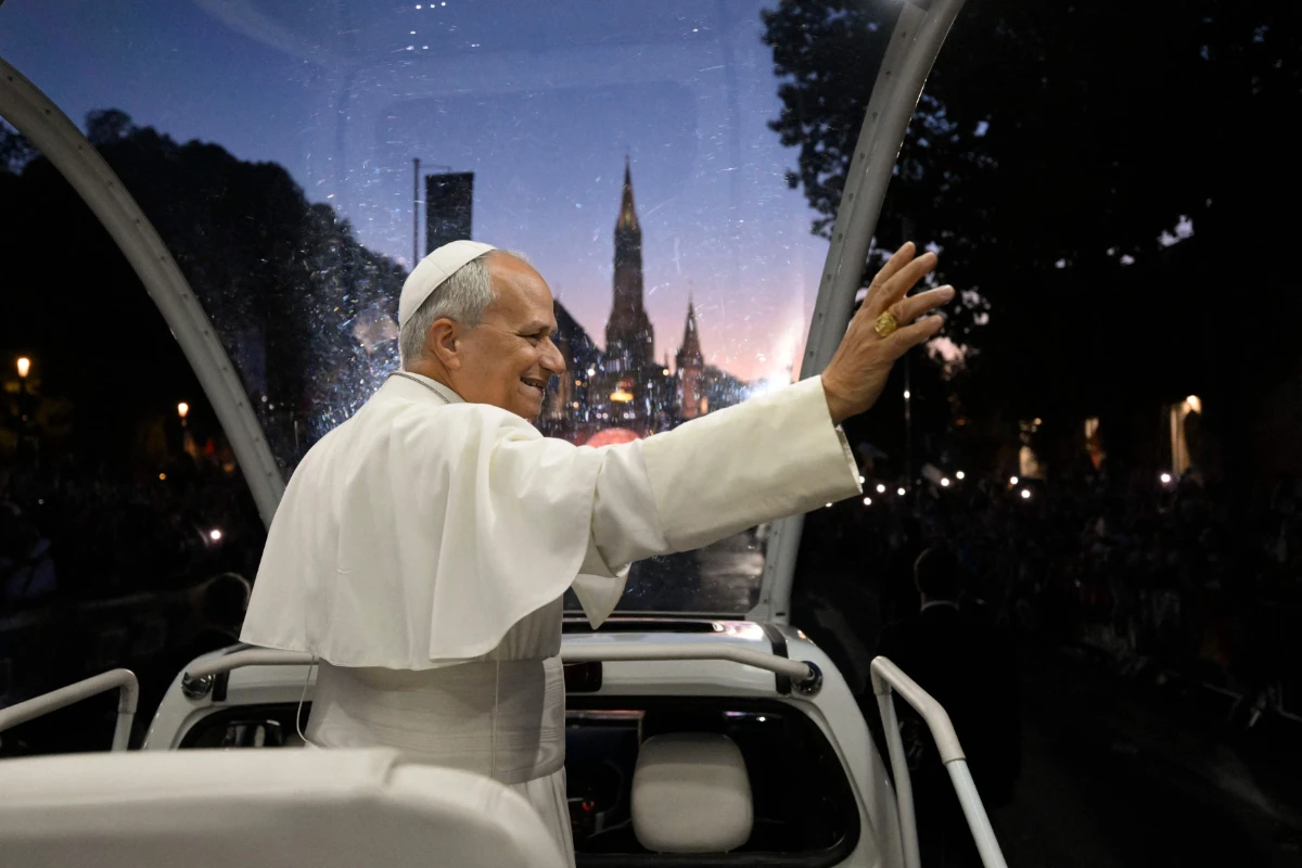 Pope Leo XIV waving from the Papamobile with the Basilica of the Immaculate Conception in the background at sunset.