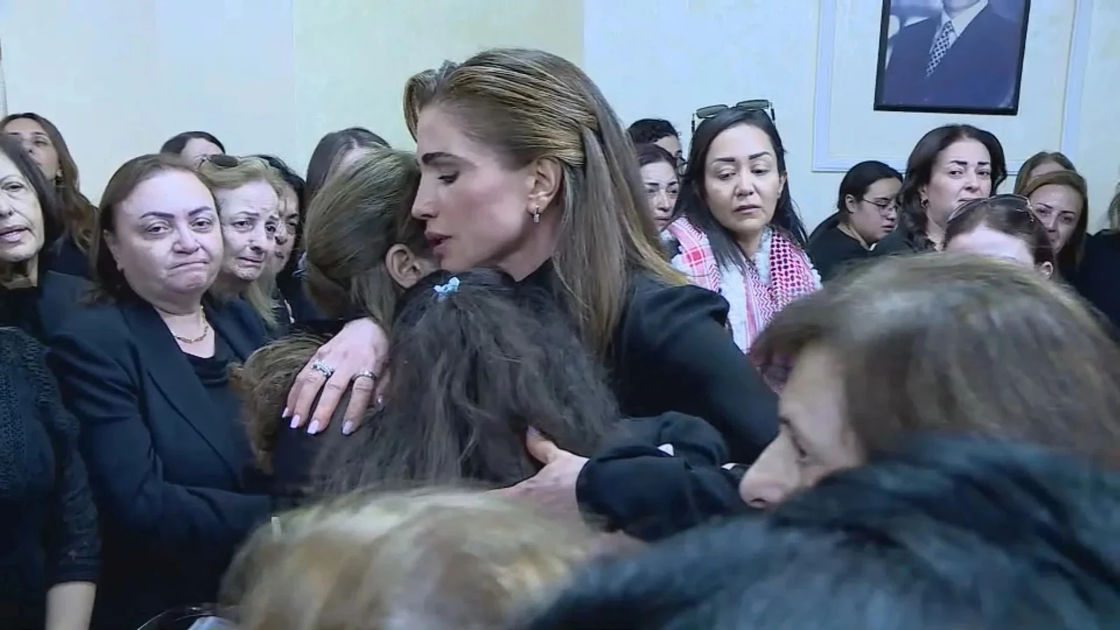 Queen Rania of Jordan offers a comforting embrace to a young girl amidst a gathering of women in mourning.