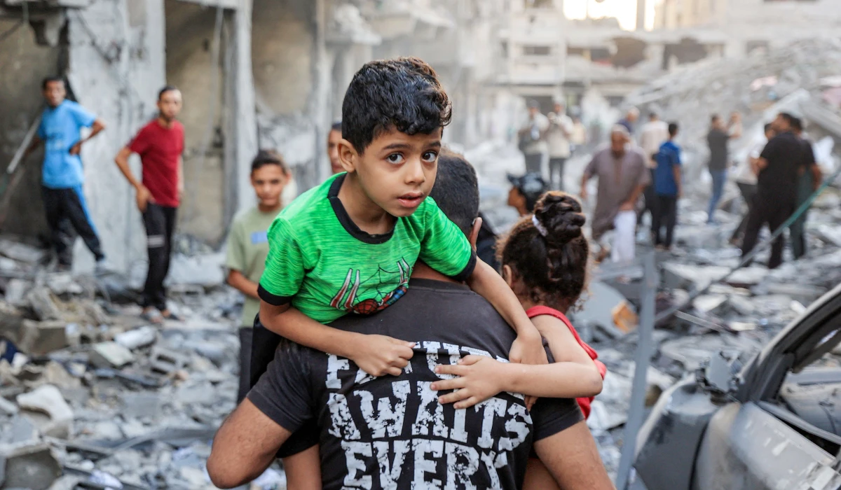 A man carries a boy near the rubble of a collapsed building as people search the site following overnight Israeli airstrikes in Gaza City on October 9, 2026. (AFP)