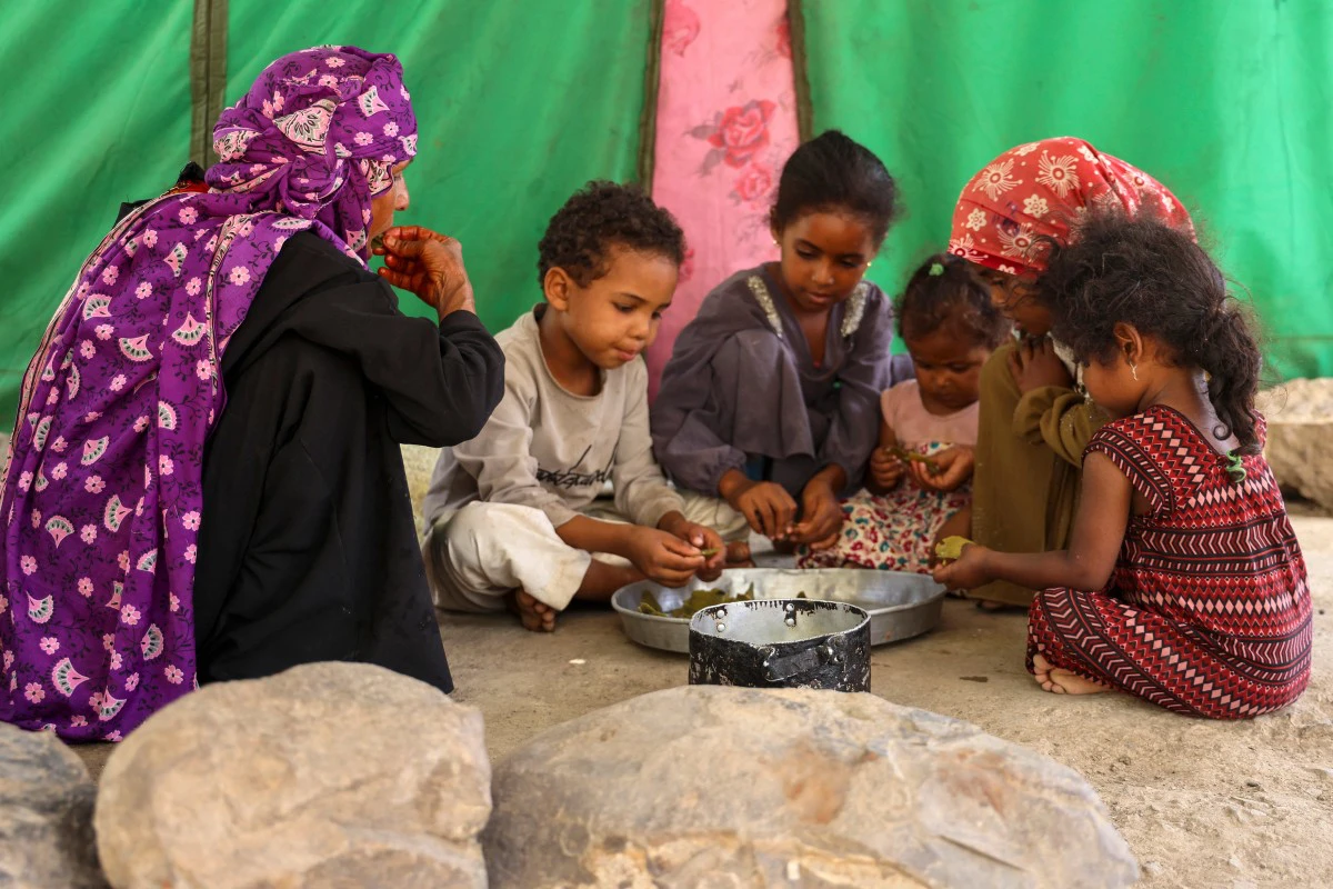 Saeedah Mohammed along with her grand-children, eat boiled tree leaves inside their makeshift tent in the Al-Manij displacement camp, near the city of Taiz in Yemen's southwest, on May 21, 2026. (AFP)