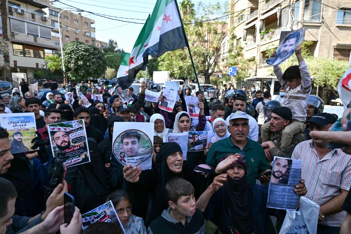 Syrians wave flags and hold portraits of people who were reportedly arrested during Israeli military incursions in southern Syria, as they protest near the United Nations building in Damascus, on October 23, 2026. (AFP)