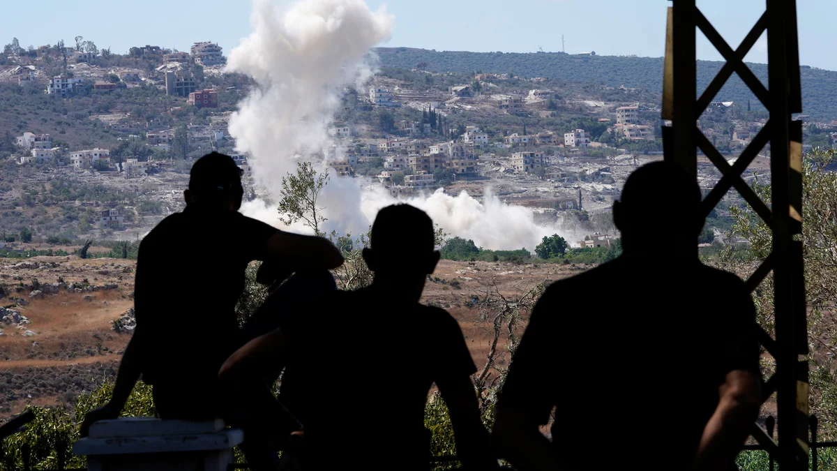 Silhouetted figures observe smoke rising from a distant village on a hillside.