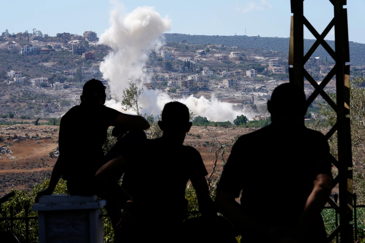 Silhouetted figures observe smoke rising from a distant village on a hillside.