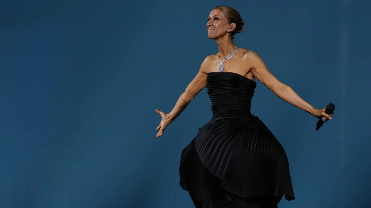 A singer in a black evening gown stands on stage with a microphone, against a blue background, striking a dramatic pose.