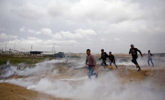 Palestinian protesters run from tear gas fired by Israeli forces during clashes following a protest along the border with Israel, East of Gaza City on April 3, 2018. (AFP)