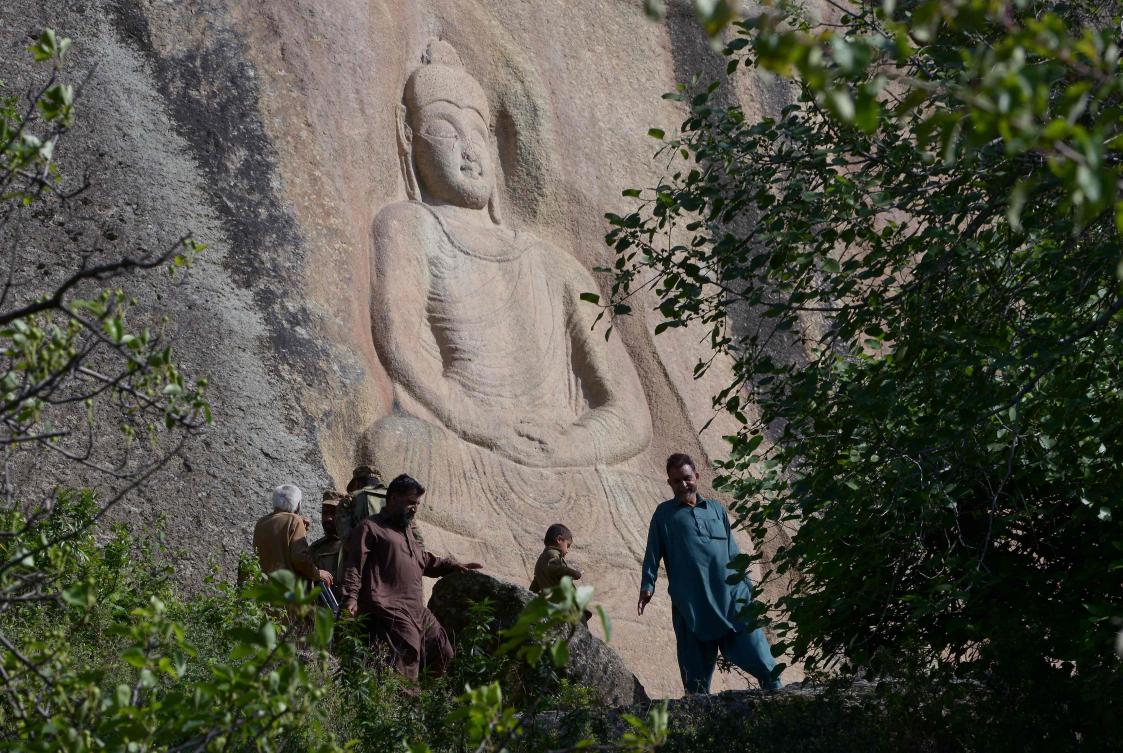 This photo taken on April 26, 2018 shows Pakistani visitors walking past the seventh-century rock sculpture of a seated Buddha carved into a mountain in Jahanabad town in the northwestern Swat Valley of Pakistan, following a restoration process conducted by Italian archaeologists after the Taliban defaced it in 2007. (AFP)