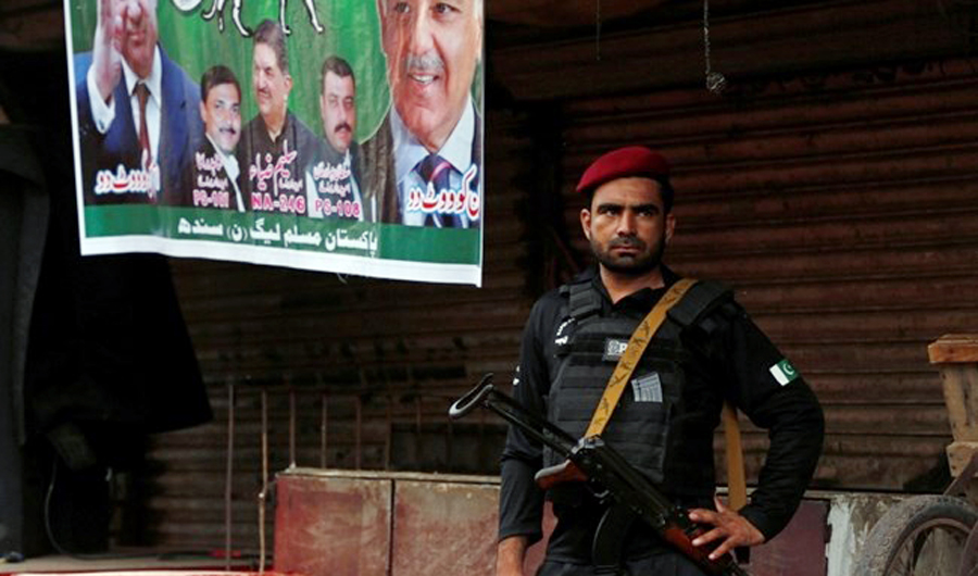 A police officer stands guard next to an electoral poster during a campaign rally ahead of general elections in the Lyari neighborhood in Karachi, Pakistan on June 26, 2018. (REUTERS)