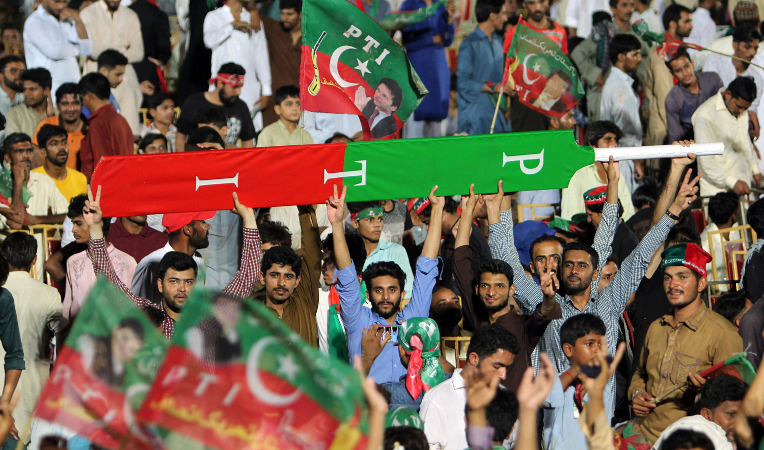 In this file photo, supporters of Pakistani cricket star-turned-politician and head of the Pakistan Tehreek-e-Insaf (PTI) Imran Khan holds a giant cricket bat with the colors and initials of the party as they cheer during a political campaign rally by Khan’s ahead of the general election in Multan on July 20, 2018. (SS MIRZA/AFP)