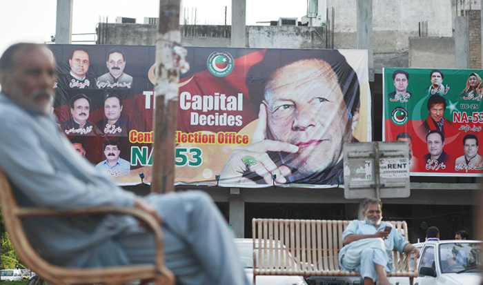 Pakistani men sit near a poster of Pakistan’s cricketer-turned-politician and head of the Pakistan Tehreek-e-Insaf party Imran Khan in Islamabad on Monday. (AFP)