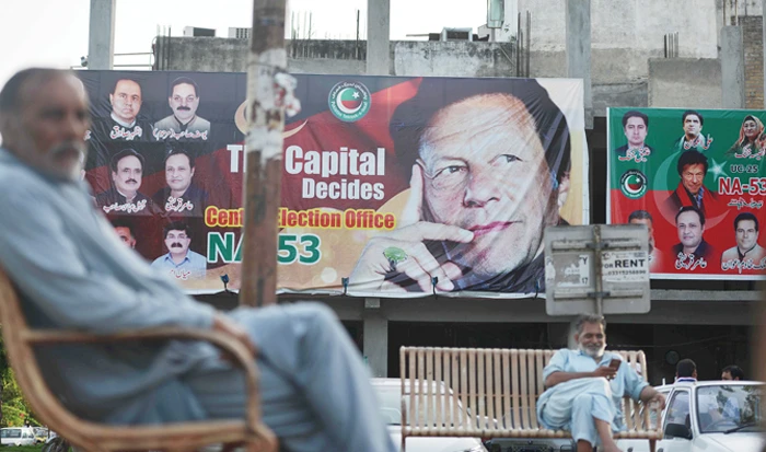Pakistani men sit near a poster of Pakistan’s cricketer-turned-politician and head of the Pakistan Tehreek-e-Insaf party Imran Khan in Islamabad on Monday. (AFP)
