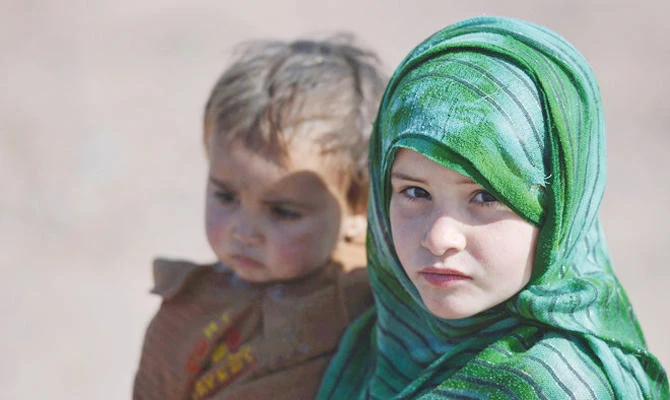 Photo Caption: An Afghan refugee girl carries her brother at a refugee camp on the outskirts of Islamabad. (AFP/File)