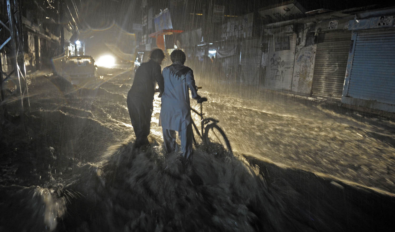 In this file photo, Pakistani men cross a flooded street during heavy monsoon rain in Quetta on Aug. 6, 2013. (AFP)