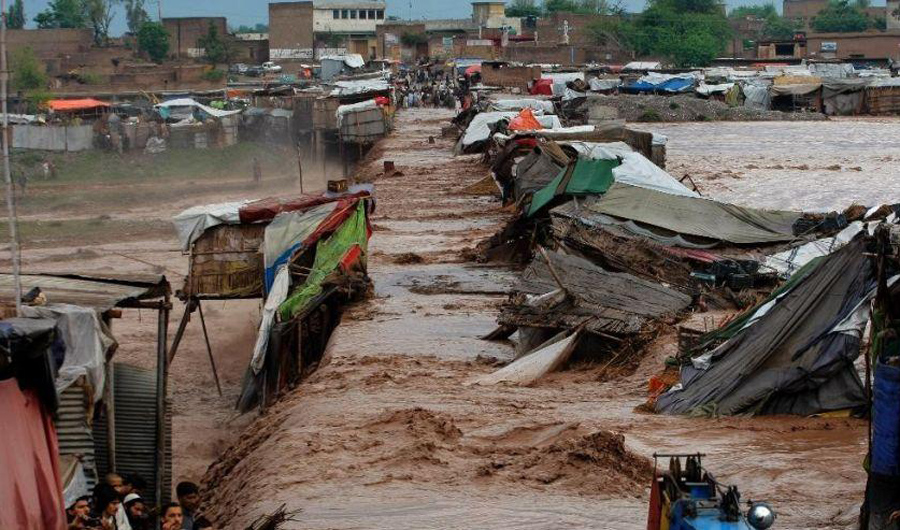 In this file photo, Pakistani villagers stand outside their homes during flash flooding on the outskirts of Peshawar, Pakistan, Sunday, April 3, 2016. (AP Photo)