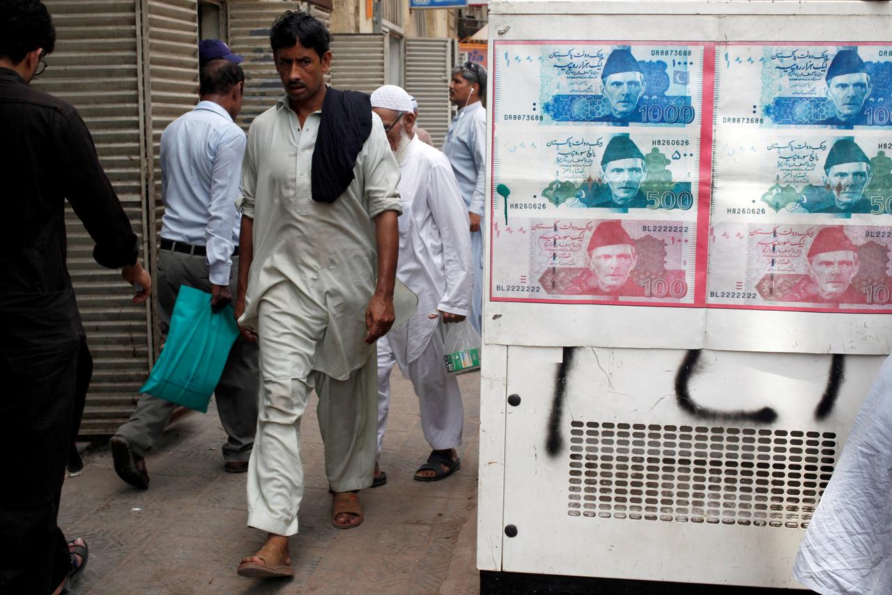 In this June 11, 2018 file photo, passersby walk past an advertisement board with photos of Pakistani rupee at a money exchange along a sidewalk in Karachi. As Pakistan negotiates with an IMF team for a bailout package, its provinces refused the fund’s demands for cash surpluses. (Reuters)
