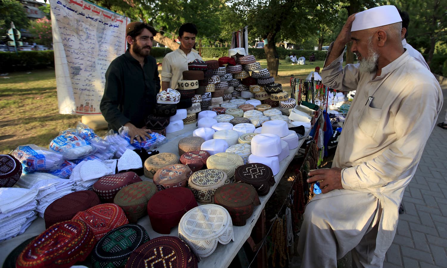 A man tries a prayer cap to buy from a stall outside a mosque in Islamabad, Pakistan, ahead of the holy fasting month of Ramazan. - Reuters