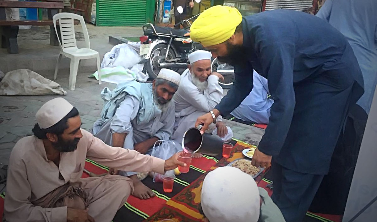 A young Sikh community leader in a yellow turban pours cold drinks for Muslims gathered in Peshawar for a sundown iftar meal hosted by the Sikh community during Ramadan on Thursday, May 16, 2019. (AN photo)