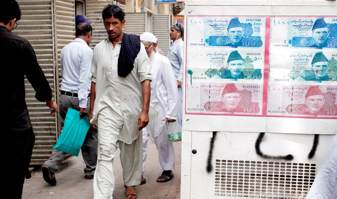 In this file photo, Passersby walk past an advertisement board with photos of Pakistani rupee at a money exchange along a sidewalk in Karachi, Pakistan on June 11, 2018. (REUTERS)