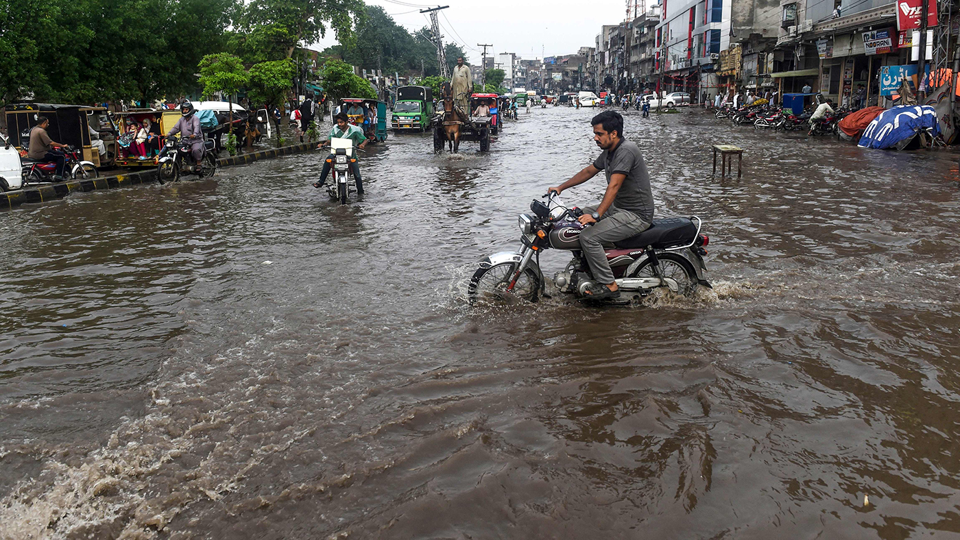 Commuters and pedestrians cross a flooded street after the monsoon rains in Lahore on July 20, 2019. / AFP / ARIF ALI