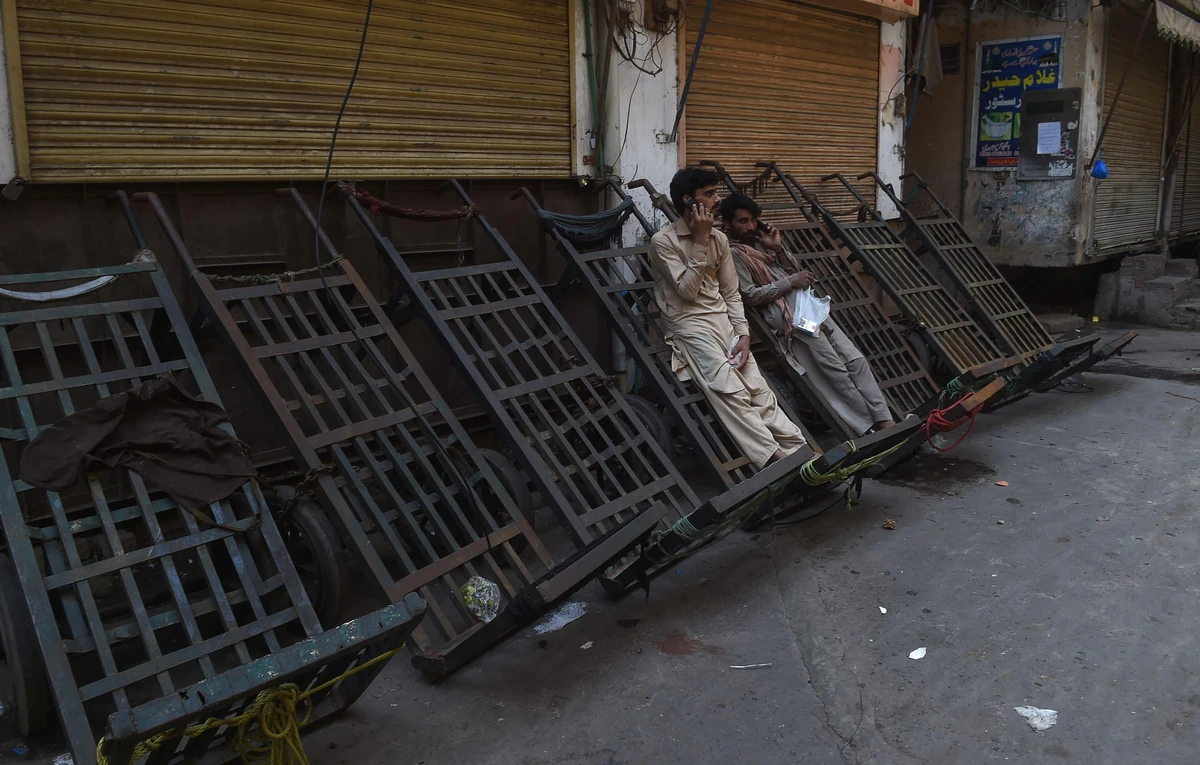 Pakistani labourers speak on a mobile phone in a shuttered market during a traders countrywide strike against the prices hike, in Lahore on July 13, 2019. (AFP)