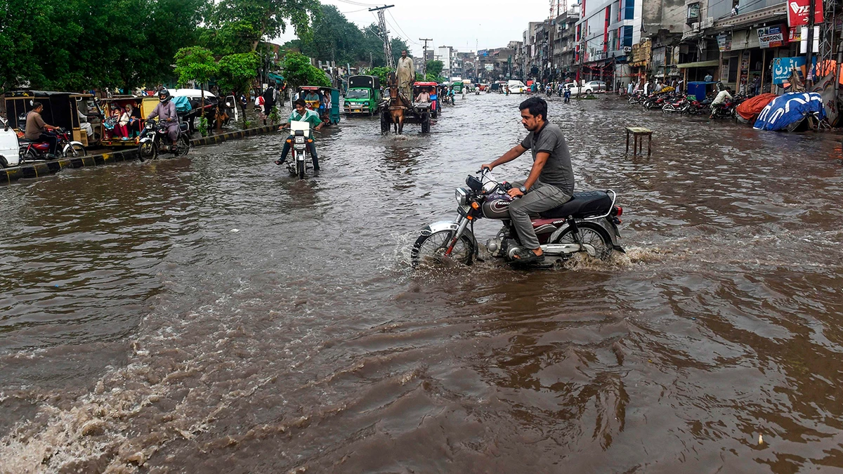 Commuters and pedestrians cross a flooded street after the monsoon rains in Lahore on July 20, 2019. / AFP / ARIF ALI