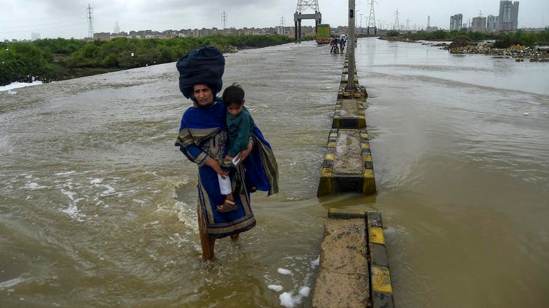 A woman holds her baby as she crosses a flooded street after heavy monsoon rains in Karachi on August 1, 2019. (File photo: AFP)